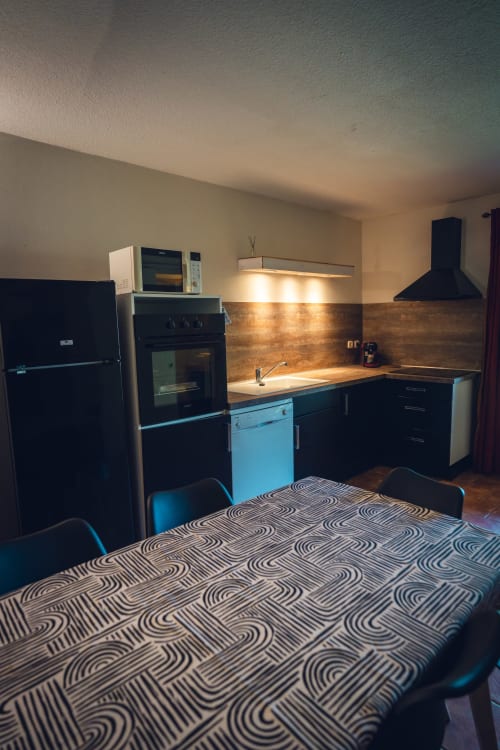 Cuisine moderne avec appareils noirs, dosseret en briques et table à manger à la villa Le Maquis Plage en Corse
