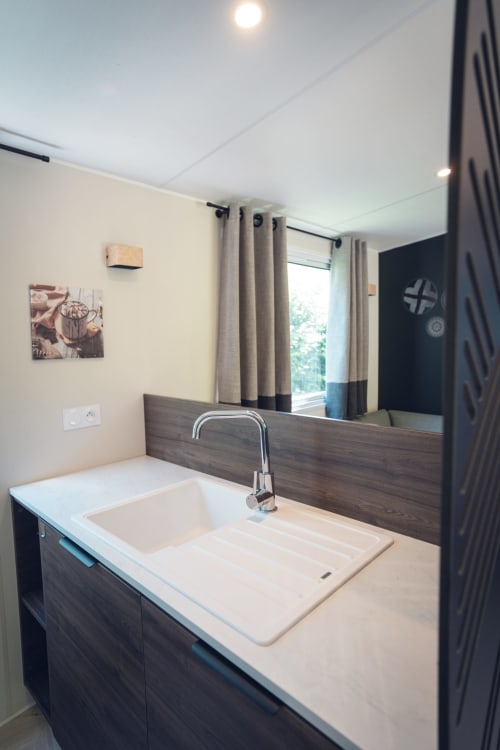 Lavabo moderne avec vanité en bois foncé, grand miroir et rideaux beige à la villa Le Maquis Plage