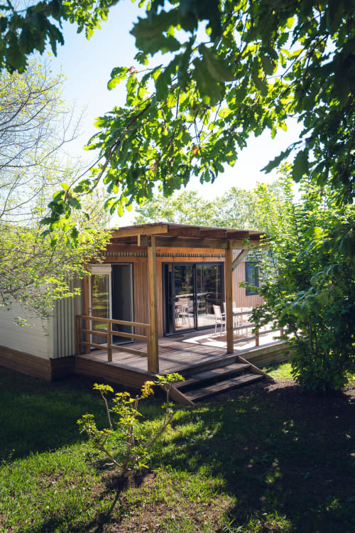 Mobil-home moderne en bois avec terrasse entourée d'arbres verdoyants à Le Maquis Plage, Poggio-Mezzana