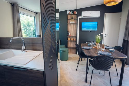 Kitchenette moderne au Le Maquis Plage avec évier, table à manger, TV et mur d'accent foncé à Poggio-Mezzana