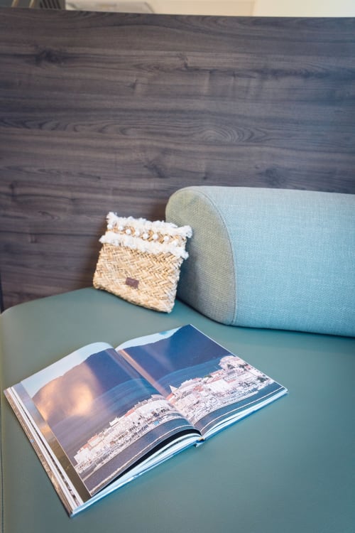 Light blue chair with woven pillow and coastal travel magazine at Le Maquis Plage hotel