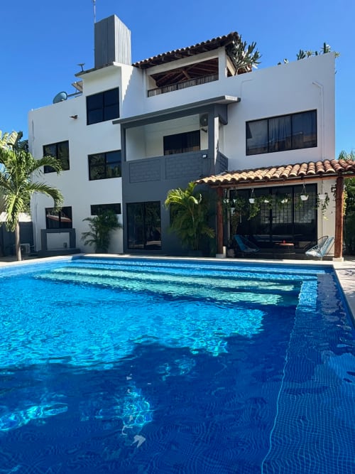 Piscina Casa Tsuki en Puerto Escondido con cabaña blanca moderna, tumbonas y vista al océano en día despejado