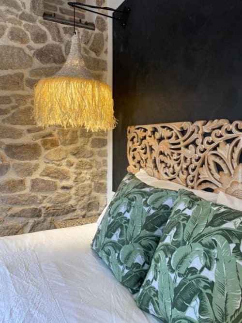 Chambre Bali du Gîte Le Moulin du Guy avec tête de lit sculptée en bois, literie botanique verte et lampe suspendue jaune