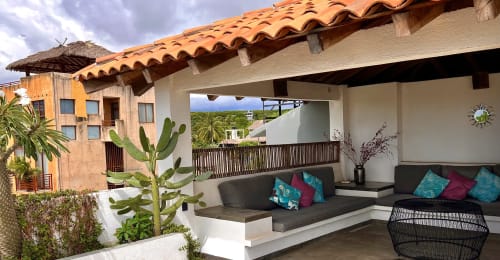 Patio de la casa Casa Tsuki con sofá gris, cojines turquesas y vistas al océano en Puerto Escondido, México
