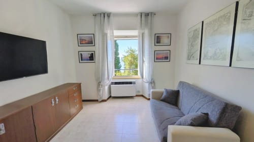 Modern apartment living room with lake view, TV, blue sofa, wooden dresser, and large window at Villa Italia