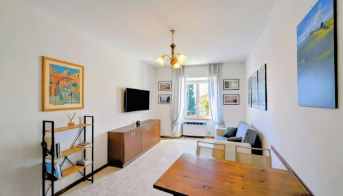 Modern apartment living room with lake view, dining table, TV, wooden shelving, and contemporary artwork at Villa Italia