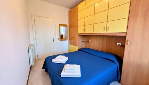 Blue bed with folded towels in cozy apartment bedroom at Villa Italia Management with wooden furnishings and lake view
