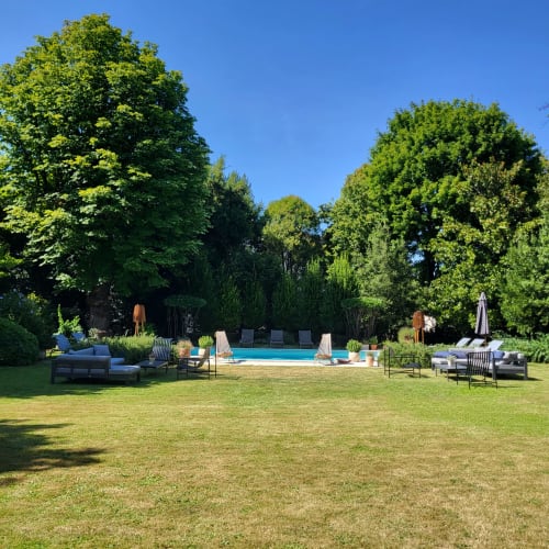 Piscine et jardin du Logis des Tourelles à Cognac avec chaises longues, arbres et ciel bleu