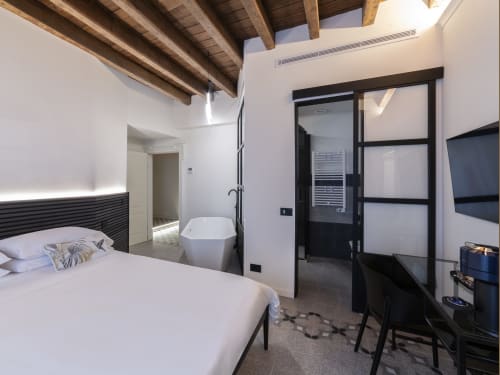 Modern bedroom at YOUnique Milano with freestanding bathtub, wooden beams, and black framed glass door