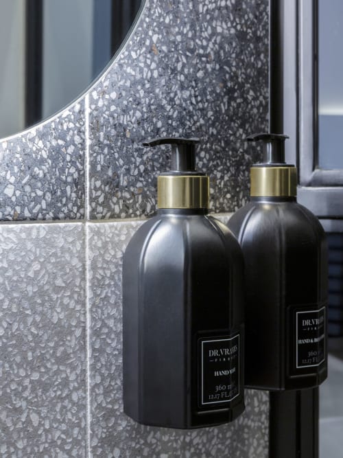 Two black Dr. Vranjes hand wash dispensers with brass accents on gray terrazzo bathroom tiles at YOUnique Boutique Rooms