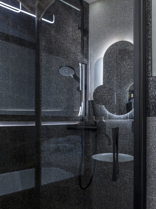 Modern black terrazzo shower with rainfall showerhead and neon lighting at YOUnique Boutique Rooms Milano