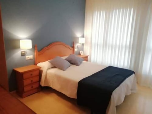 Acogedora habitación doble en Pensión San Vicente con cama de madera, mesitas de noche, lámparas y vistas a las montañas a través de persianas verticales