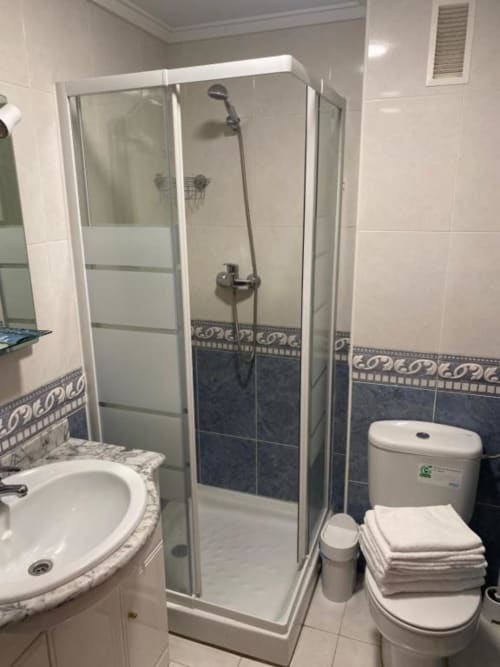 Baño moderno y limpio en Pensión San Vicente con ducha de cristal, lavabo blanco, inodoro y detalles en azulejos azules