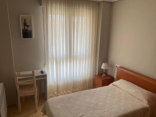 Habitación individual de la Pensión San Vicente con cama, escritorio, muebles de madera y vistas a las montañas a través de persianas verticales
