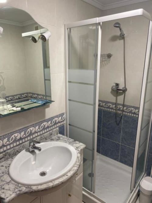 Baño moderno en la Pensión San Vicente con lavamanos redondo, mampara de ducha y detalles decorativos en azulejos