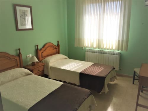 Habitación doble luminosa en Pensión San Vicente con dos camas individuales, paredes verdes, muebles de madera y luz natural
