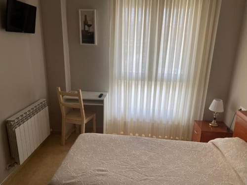 Acogedora habitación individual en Pensión San Vicente con cama, escritorio, vistas a la montaña a través de persianas, TV y radiador de calefacción