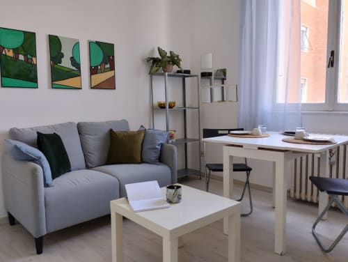 Soggiorno moderno a Campagnano di Roma con divano grigio, tavolino bianco, zona pranzo e finestre con vista sul giardino