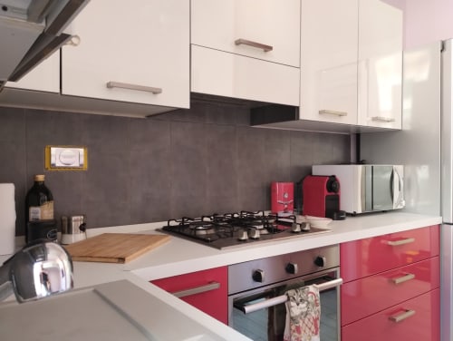 Cucina moderna con mobili rossi e bianchi, piano cottura nero e rivestimento in piastrelle grigie presso l'appartamento La Casetta di Nonna Ro