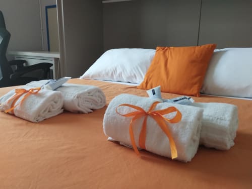 Asciugamani bianchi arrotolati con nastri arancioni su coperta arancione in camera da letto di appartamento a Roma