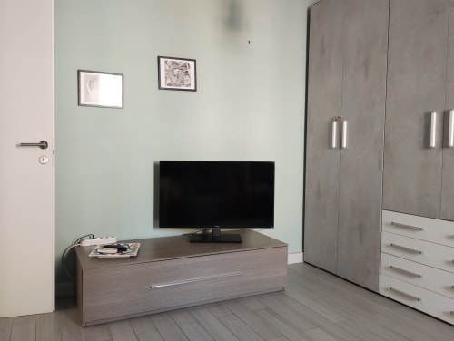 Camera da letto moderna con TV schermo piatto su scrivania in legno, guardaroba grigio e arredamento minimalista a Campagnano di Roma