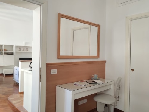 Scrivania moderna e specchio in appartamento romano con testata in legno, sedia bianca e zona lavoro con vista sulla città