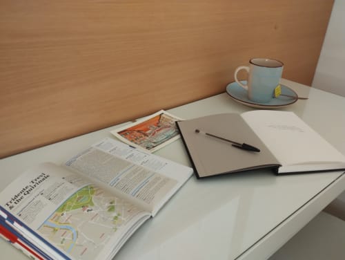 Spazio di lavoro in appartamento a Roma con rivista aperta, taccuino, penna e tazza di tè sulla scrivania