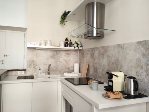 Cucina bianca moderna con cappa in acciaio inox, paraschizzi in piastrelle grigie, macchina da caffè e bollitore nell'appartamento di Roma