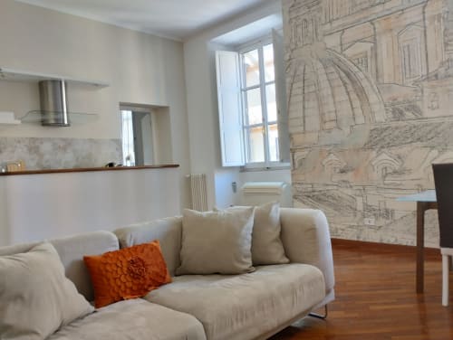 Soggiorno di un elegante appartamento romano con divano beige, cuscino arancione, pavimento in legno, carta da parati architettonica e vista sulla città
