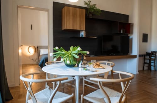 Zona pranzo di moderno appartamento con tavolo rotondo bianco, sedie in legno e fiori freschi a Roma, Italia