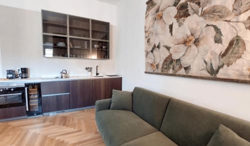 Moderno living a Campagnano di Roma con divano verde salvia, cucina con ante scure e arte floreale
