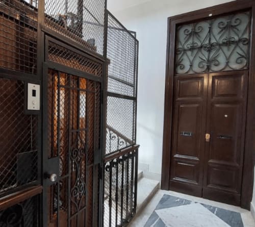 Elegante ingresso di appartamento a Roma con porte in legno ornato, cancellate di sicurezza in metallo e pavimenti in marmo