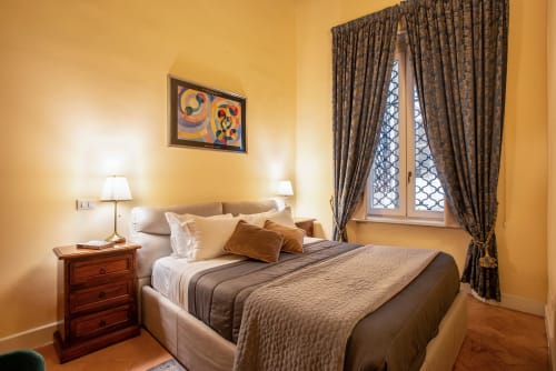 Camera da letto gialla e accogliente alla Residenza Sinibaldi di Roma con letto matrimoniale, comodino in legno, tende decorate e quadri incorniciati
