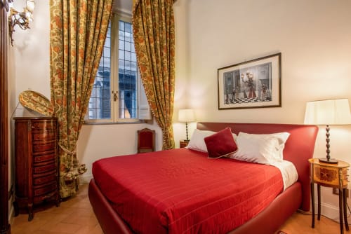 Elegante camera da letto presso Residenza Sinibaldi a Roma con biancheria rossa, tende dorate, mobili antichi e vista sulla città
