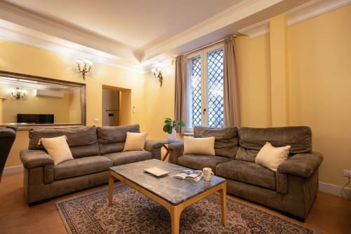 Elegante soggiorno della Residenza Sinibaldi a Campagnano di Roma con divani in pelle marrone, pareti gialle e vista sulla città