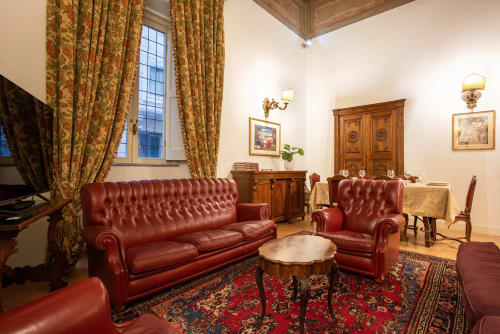 Elegante soggiorno con divano e poltrona in pelle rossa, drappeggi ornati e mobili in legno a Residenza Sinibaldi, Roma