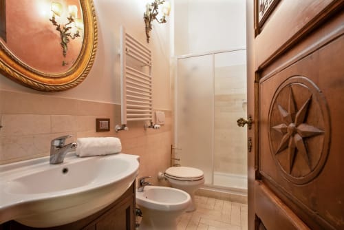 Elegante bagno della Residenza Sinibaldi con piastrelle in terracotta, porta in legno, specchio ornato, lavandino, wc, bidet e vetro