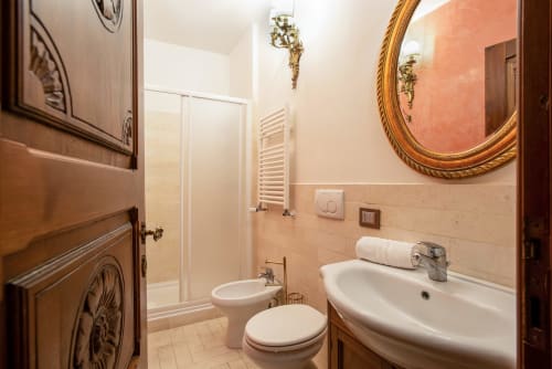Elegante bagno della Residenza Sinibaldi a Roma con lavabo su colonna, wc, doccia, specchio dorato ornamentale e piastrelle color pesca caldo
