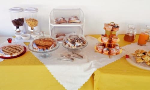 Colazione di B&B Villa Matari con pasticcini, torte, succhi e prodotti da forno su tovaglie gialle e bianche