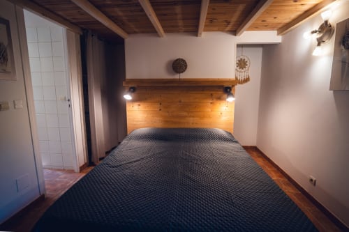 Modern hotel bedroom at Le Maquis Plage in Poggio-Mezzana with wooden headboard, dark bedding, and rustic ceiling beams.