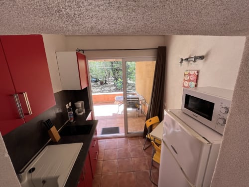 Modern kitchen at Le Maquis Plage hotel in Poggio-Mezzana with red cabinetry, black countertop, and patio access