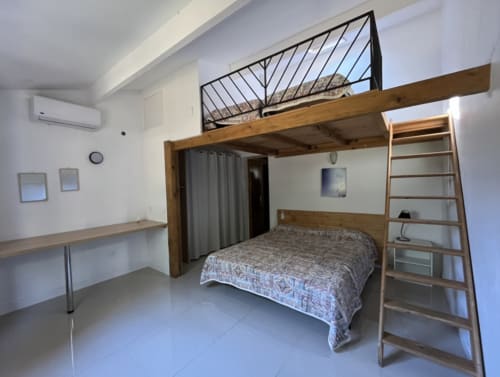 Modern loft bedroom at Le Maquis Plage with wooden mezzanine bed, work desk, and ladder in Poggio-Mezzana