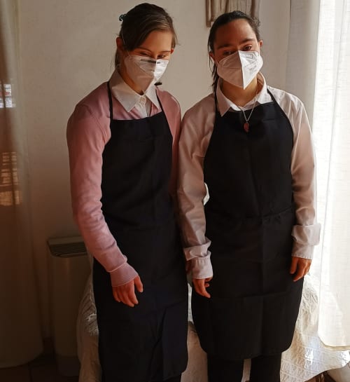 Due membri dello staff della Corte delle Giuggiole B&B a Cologna Veneta indossano grembiuli neri e mascherine protettive