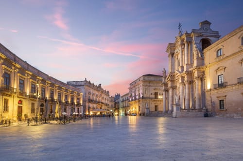 Piazza storica siciliana al crepuscolo con chiesa barocca e palazzi illuminati vicino a Fontane Bianche
