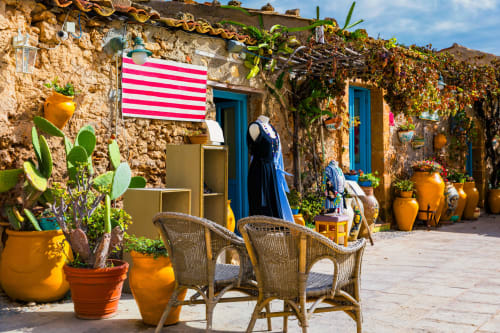 Cortile in pietra rustica del B&B Villa Matari a Fontane Bianche con sedie in vimini, porte blu e vasi in terracotta