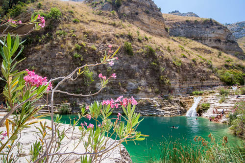 Fiori rosa si affacciano su acque turchesi e scogliere rocciose a Villa Matari a Fontane Bianche, Sicilia