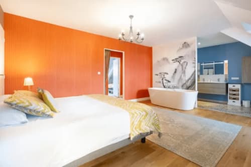 Helles Schlafzimmer in der Suite Les logis de Kergoulou in Concarneau mit orangefarbener Akzentwand, freistehender Badewanne und Holzausstattung