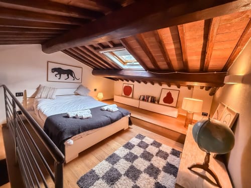 Camera da letto loft a Cognaia, Arezzo con travi in legno a vista, lucernario, letto matrimoniale, tappeto a quadri e comfort moderni