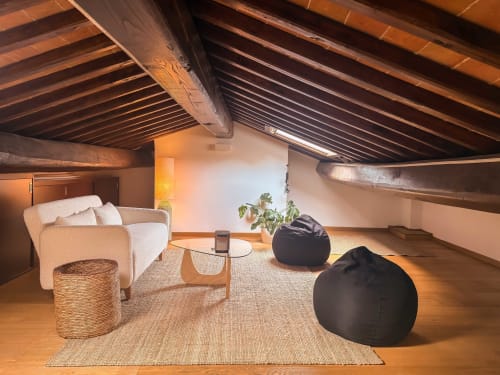 Loft Cognaia ad Arezzo con travi in legno a vista, divano color crema, pouf e arredamento minimalista su pavimenti in legno