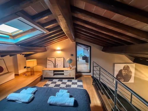 Camera da letto in loft moderno a Cognaia Loft ad Arezzo con travi in legno a vista, lucernario, letto blu, scrivania e arredamento minimalista